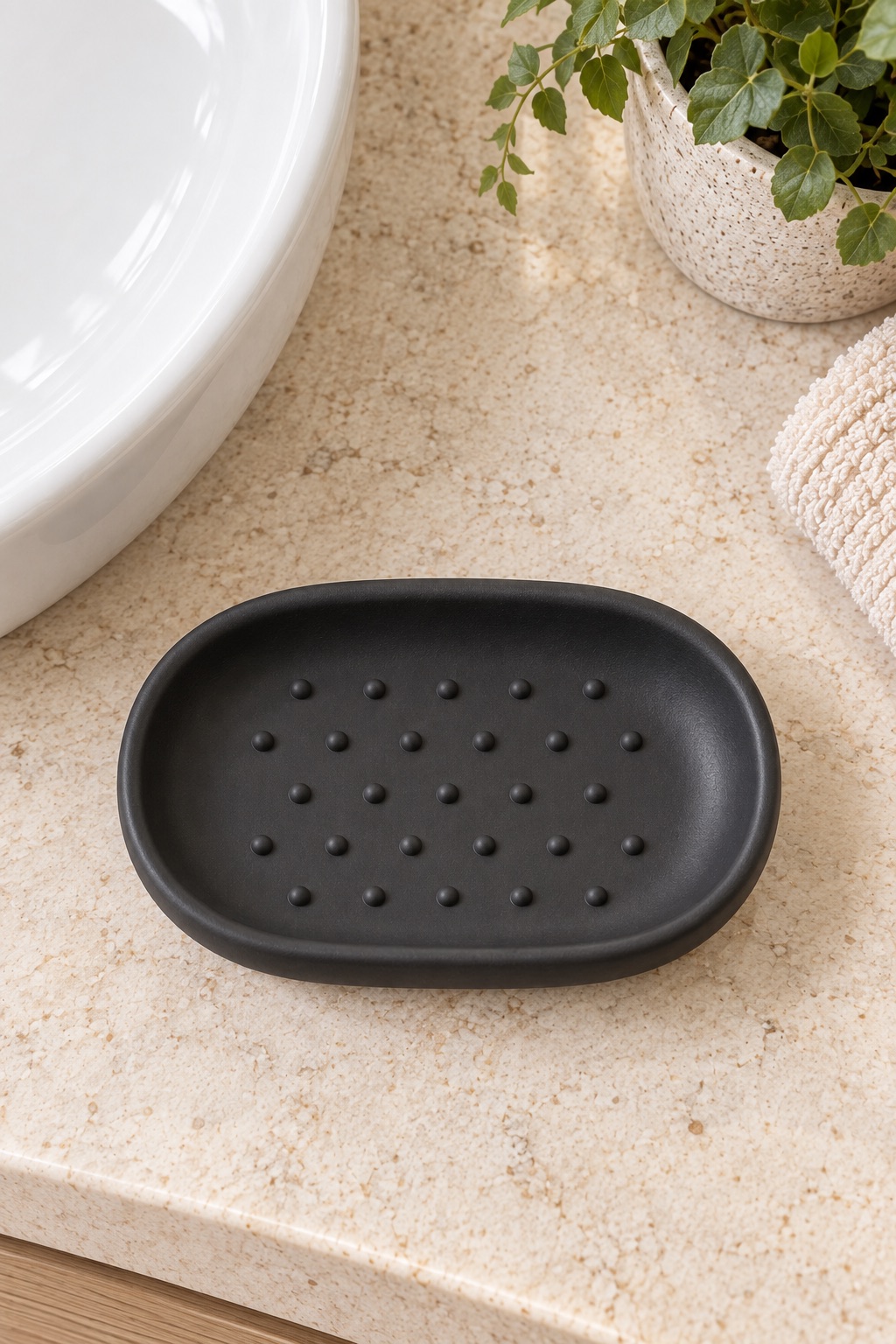 AI-generated visualization approximating the design of the Umbra Junip Oval Soap Dish, Black beside a guest-bathroom sink.